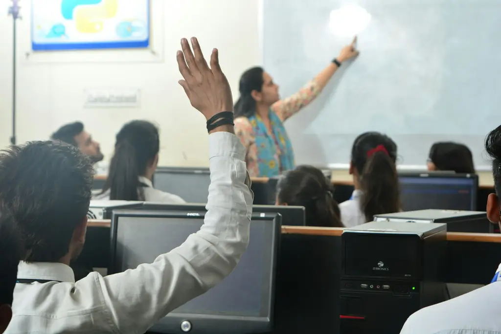 Bilgisayar sınıfında tahtadaki öğretmene soru soran öğrenciler